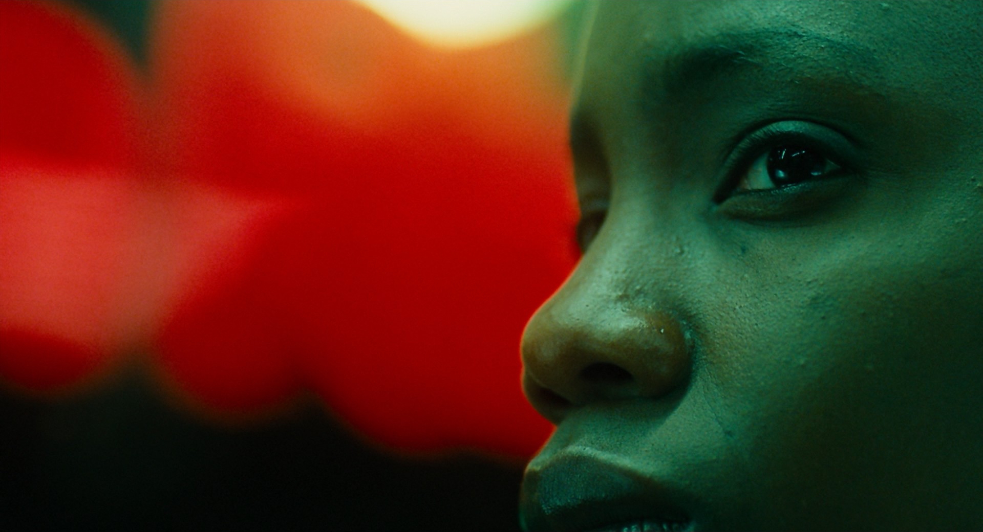 An extreme close-up of a woman's face in profile at the right, beside a large blurred red shape, in green tones